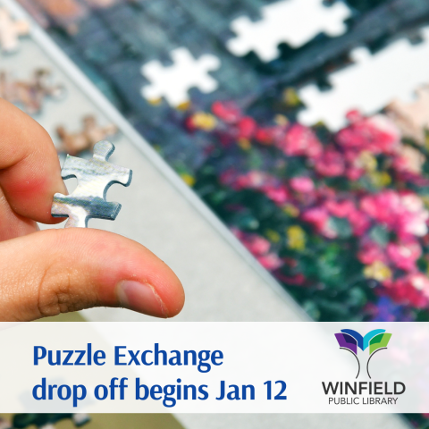 a hand holding a puzzle piece with a partially completed jigsaw puzzle in the background