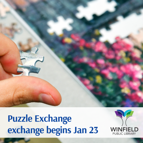 a hand holding a puzzle piece with a partially completed jigsaw puzzle in the background