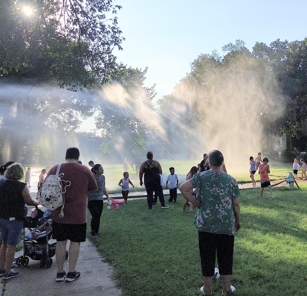 people walking through misty spray of fire hose . summer splash party